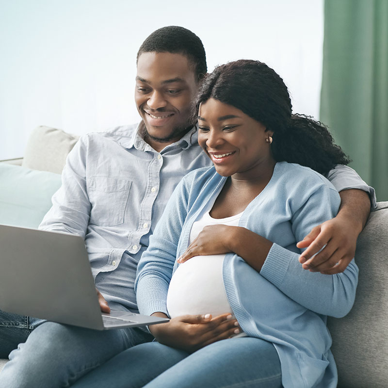 A pregnant couple looking at their laptop