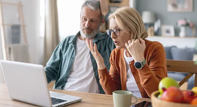 Couple looking at account on laptop and seeing they've been scammed